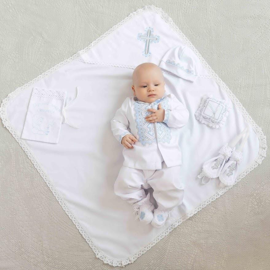 Baby in white outfit with blue accents lying on a decorative blanket