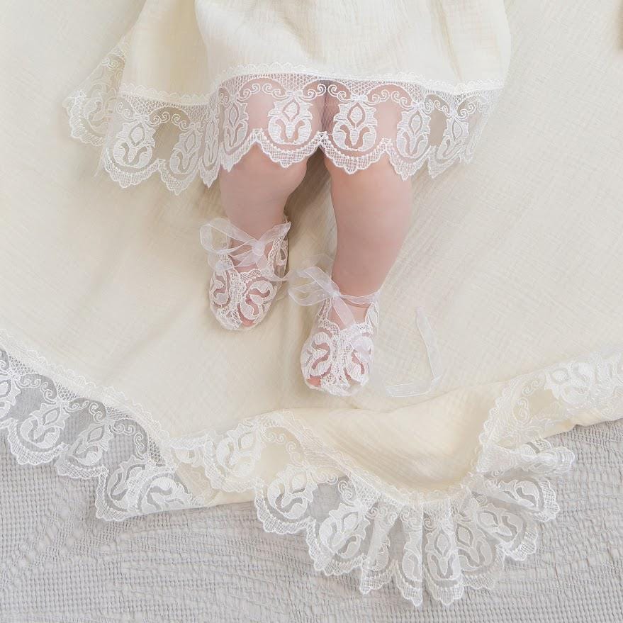 Baby girl wearing ivory muslin baptism dress with lace details