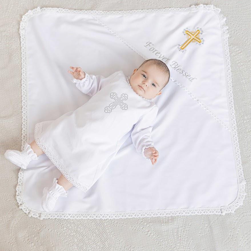 Baby lying on a white christening blanket with lace trim, embroidered cross, and personalized text for baptism ceremony.